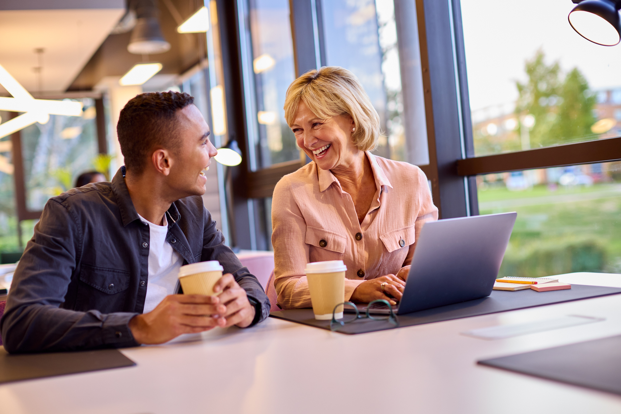 Mature Businesswoman Mentoring Younger Male Colleague Working On Laptop At Desk