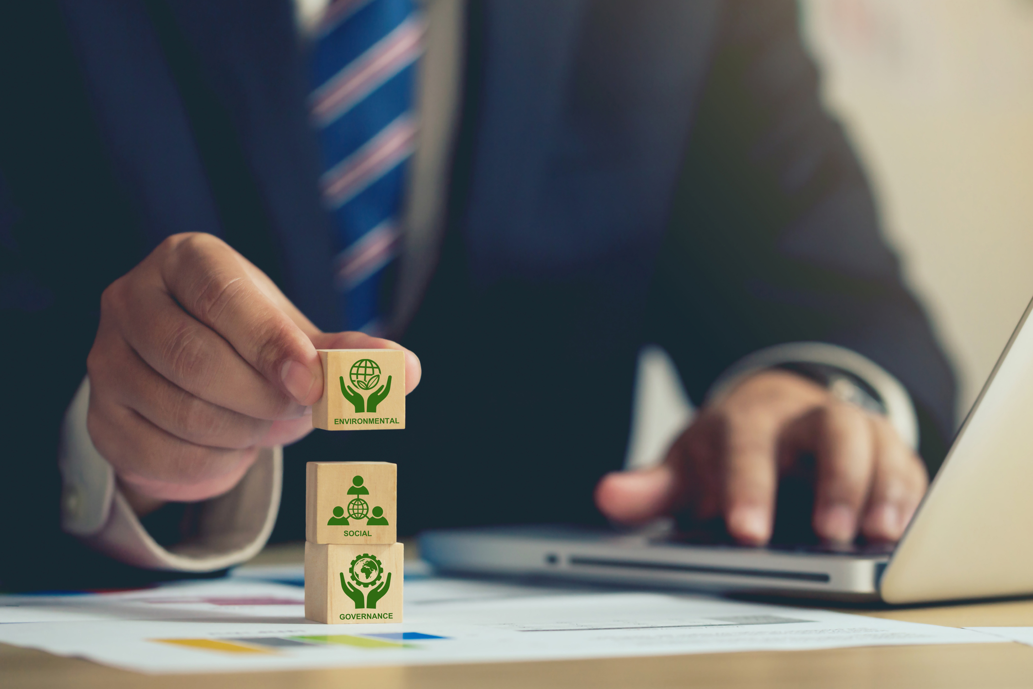 ESG concept of environmental, Businessman hand holding wooden cube block with ESG icon with copy space, Businessman Planing an ESG Project on laptop. Green Energy, Renewable and Sustainable Resources.