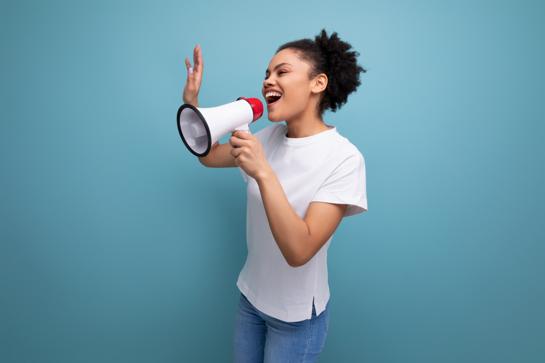 young brunette latin woman in a white t-shirt uses a loudspeaker to announce important news on the background with copy space.